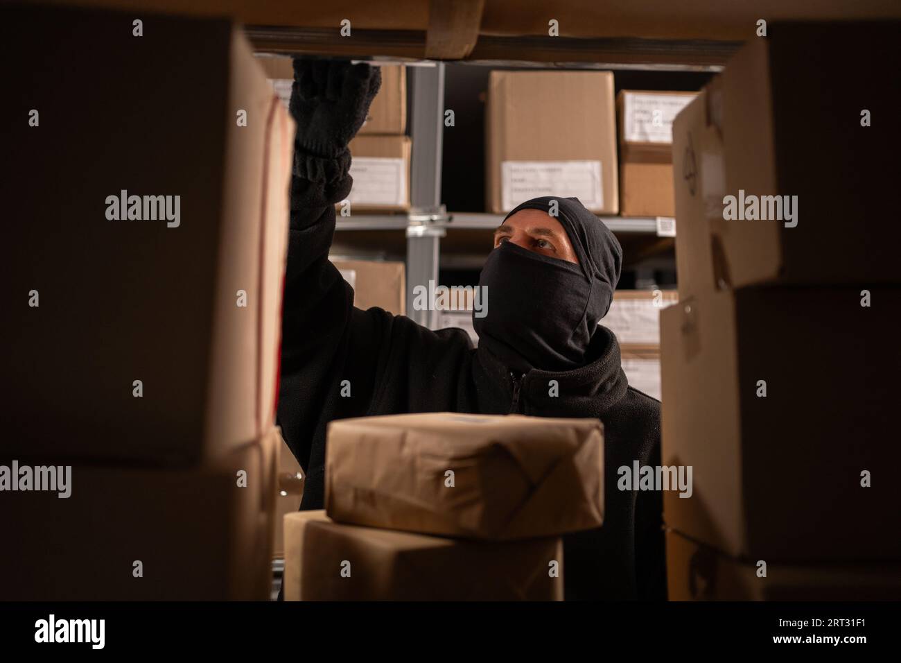 Dieb in einer schwarzen Maske stiehlt eine Schachtel Parzelle in einem Lager, Nahaufnahme. Zur Problematik des Diebstahls von Postpaketen Stockfoto
