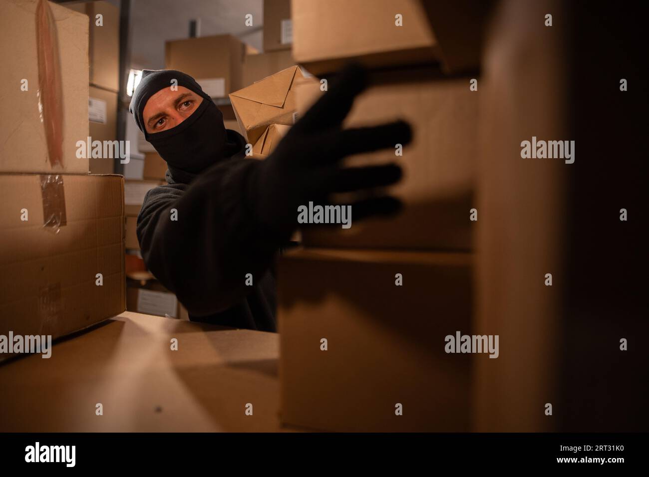 Dieb in schwarzer Sturmhaube stiehlt nachts mit einem Paket in einem Lagerhaus. Konzept von Sicherheitsproblemen in Lagerhäusern und Stores. Stockfoto