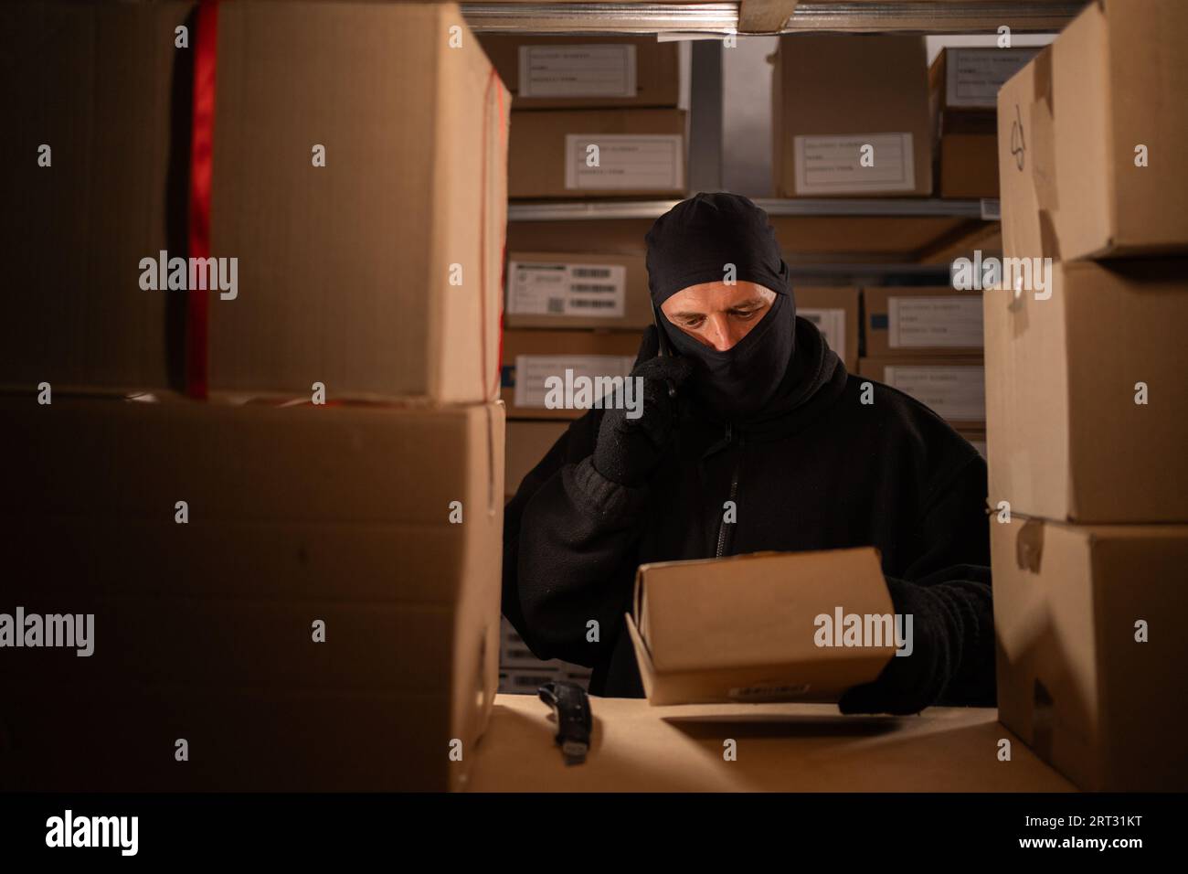 Der Dieb, der eine Kiste in einem Lagerhaus klaut, ruft nachts auf dem Handy an. Zur Problematik des Diebstahls von Gütern und Paketen an der Post. Stockfoto