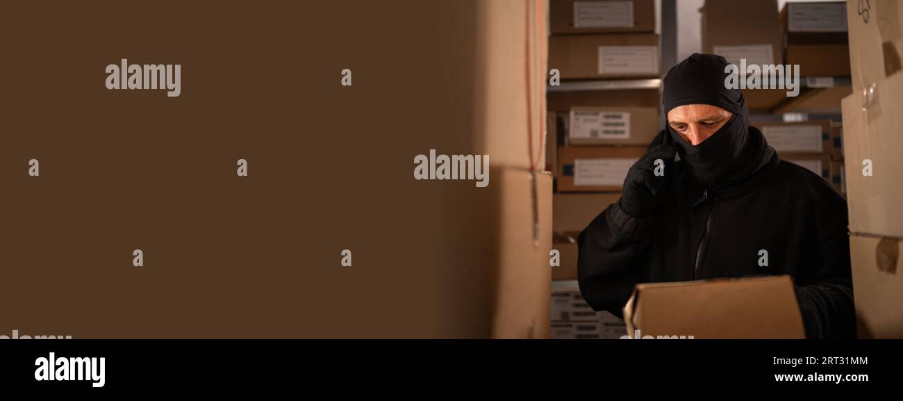 Der Dieb, der eine Kiste in einem Lagerhaus klaut, ruft nachts auf dem Handy an. Zur Problematik des Diebstahls von Gütern und Paketen an der Post Stockfoto