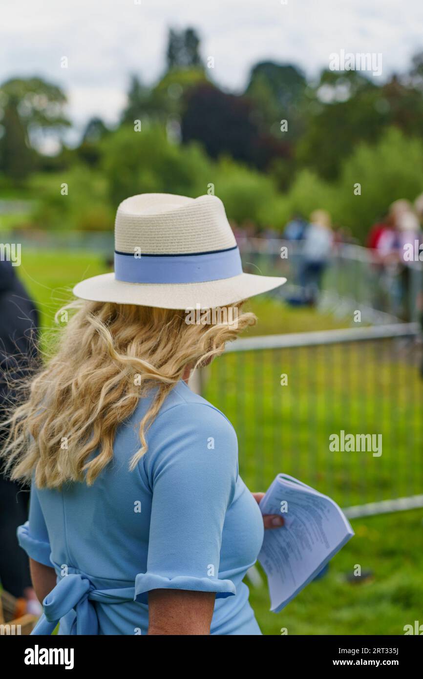 Frau mit langen blonden Haaren bei der Ripley Show, North Yorkshire, England; trägt einen Orford Fedora mit einem hellblauen Band und einem passenden Kleid. Stockfoto