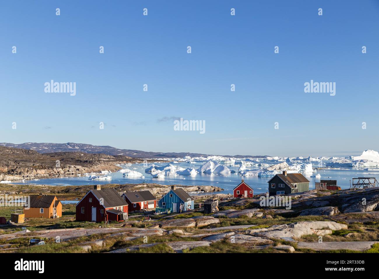 Rodebay, Grönland, 09. Juli 2018: Bunte Holzhäuser mit Eisbergen im Hintergrund. Rodebay, auch bekannt als Oqaatsut, ist eine Fischersiedlung Stockfoto
