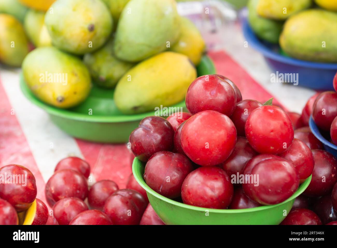 Tisch mit einem Korb Pflaumen und Mangos auf dem Straßenmarkt Stockfoto