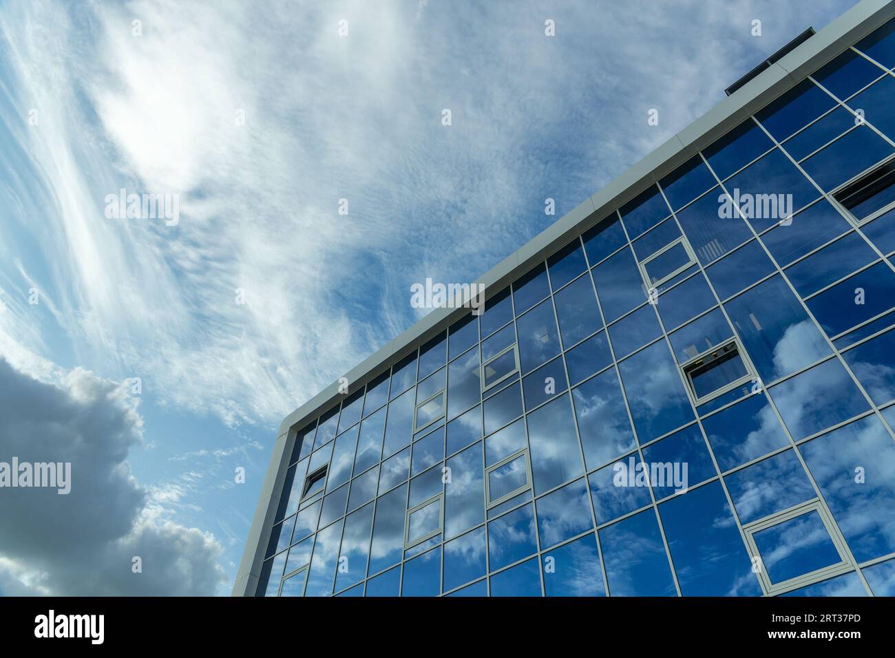 Architektonisches Detail der Fassade mit mehrfachen Reflexionen des bewölkten Himmels und der Sonne. Außenansicht eines modernen Gebäudes. Abstrakter Hintergrund der Architektur Stockfoto