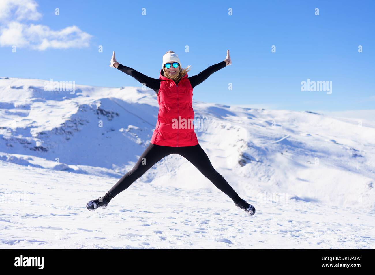 Fröhliche Frau in warmer Kleidung, die in der Luft auf Schneelandschaft springt Stockfoto