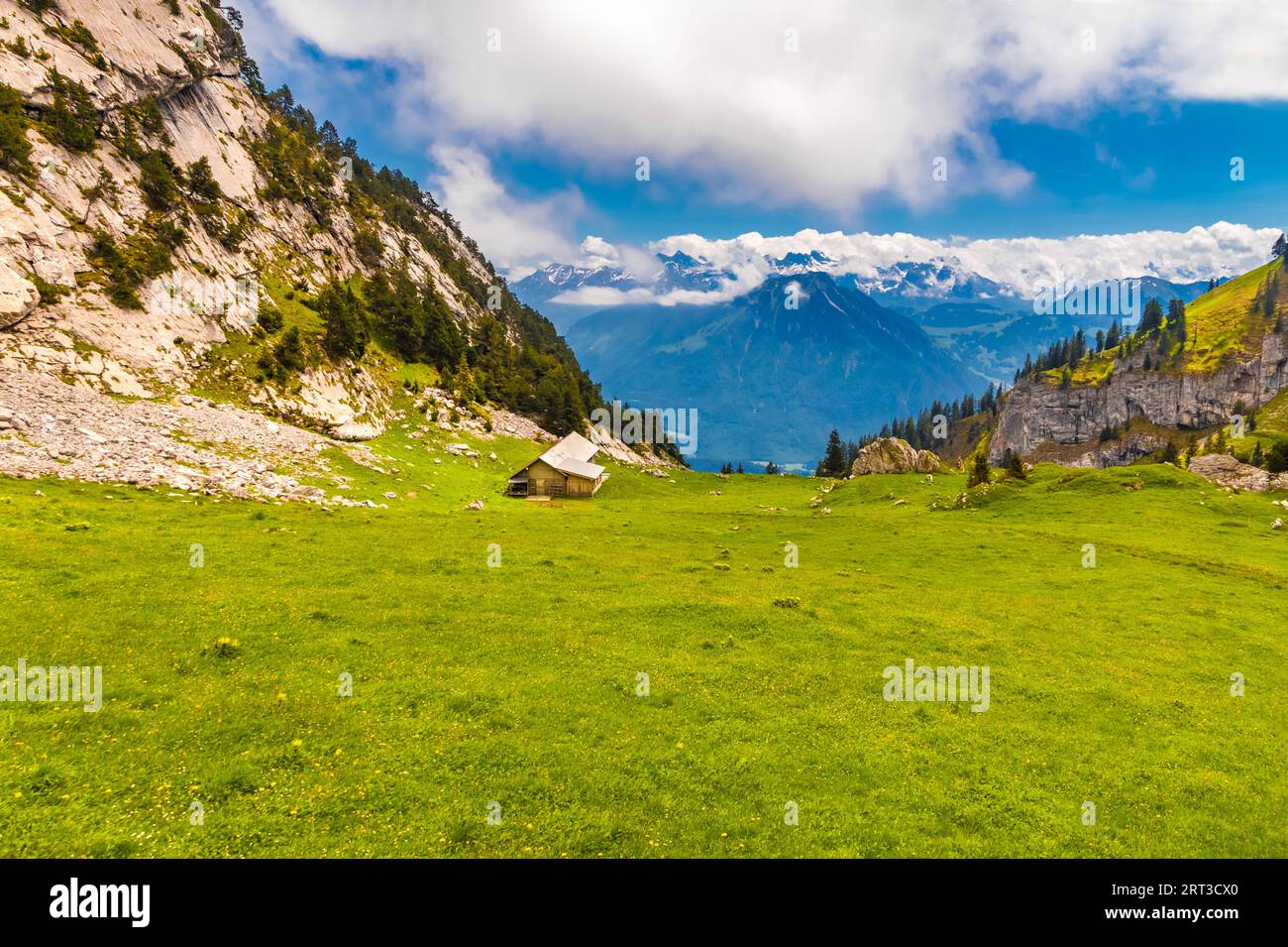 Malerischer Blick auf eine typische Berglandschaft mit einer hölzernen Almhütte umgeben von saftigen Wiesen und wunderbarem Blick auf die Berge aus der Ferne und... Stockfoto