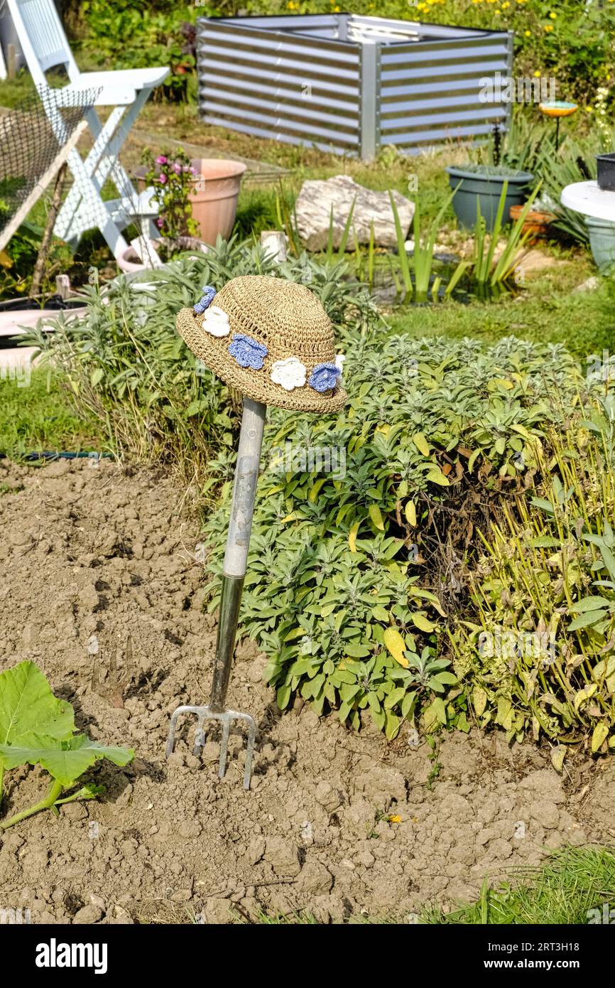 Strohhut für Damen mit Blumenmotiv, der auf dem Griff einer Gartengabel in britischem Kleinod ruht Stockfoto