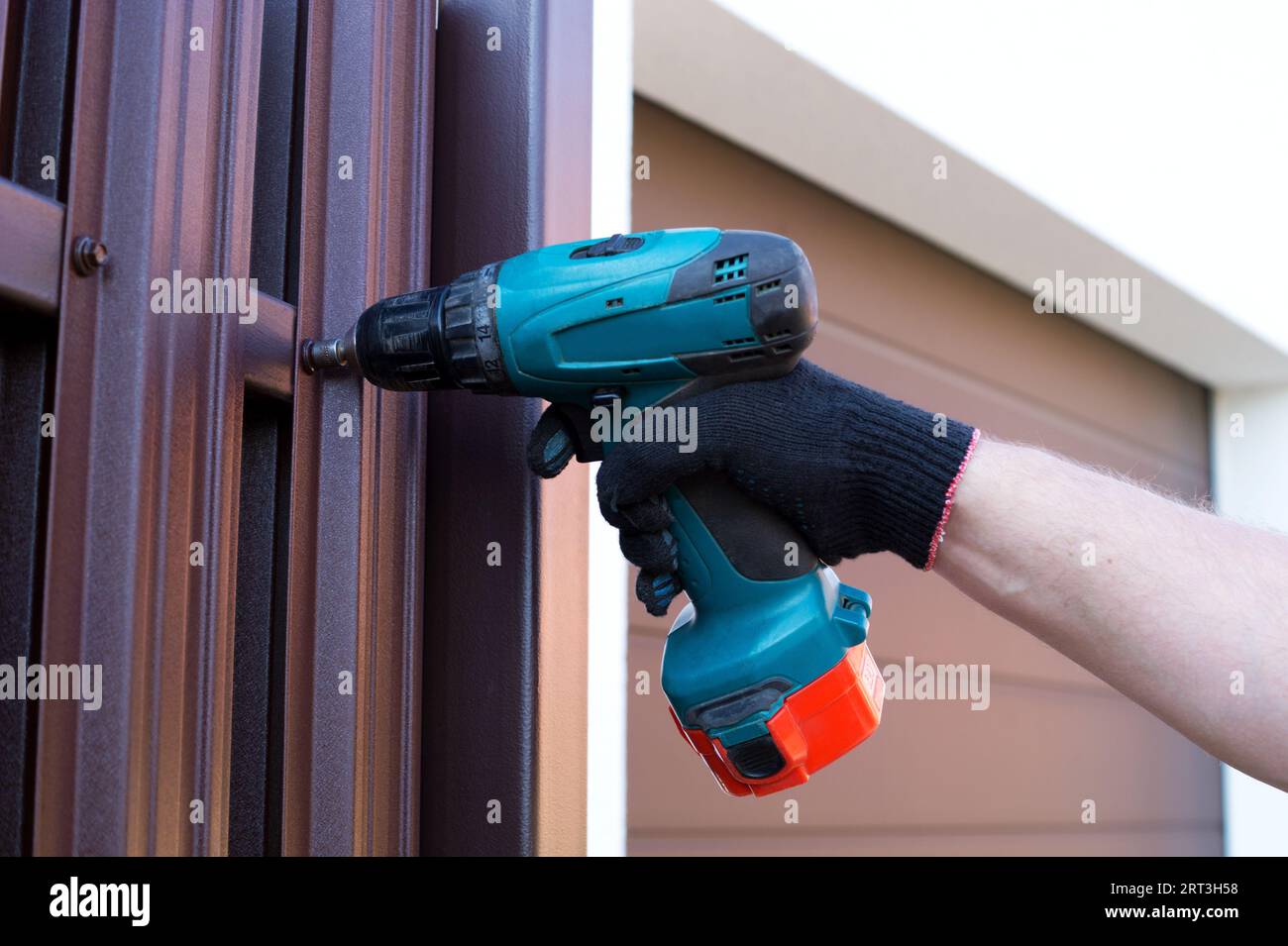 Schrauben von Dachschrauben mit einem kabellosen Elektroschrauber in einen Metallzaun. Zaun, Einbau des Zauns. Nahaufnahme. Automatische Metallwalze Stockfoto