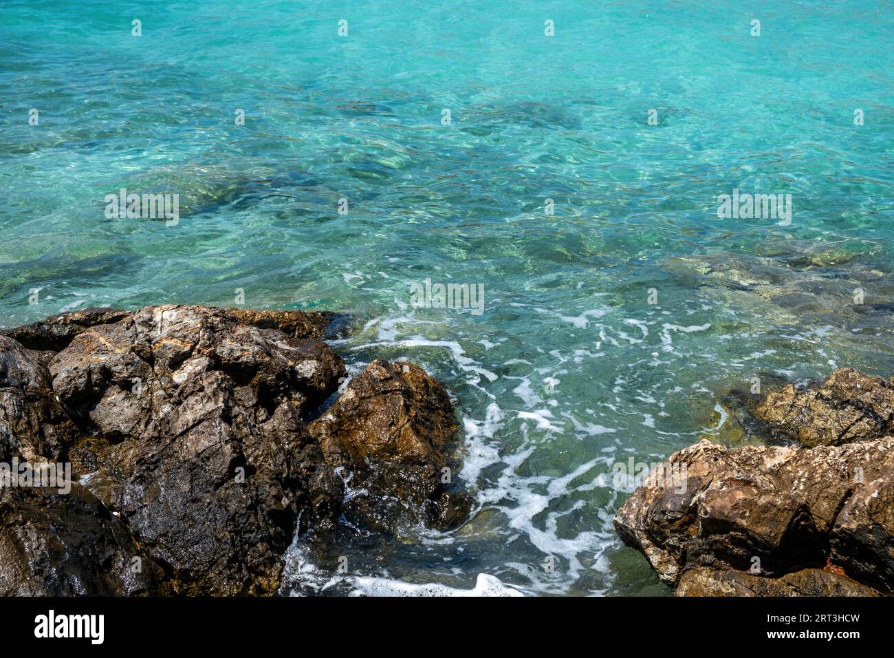 Schaumige Wellen brechen auf dem Felsen in klarem, transparentem, türkisfarbenem Meerwasserhintergrund. Griechenland Agistri Insel Aponisos Strand. Ansicht über Stockfoto