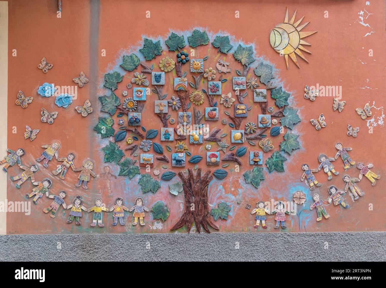 Detail einer keramischen Wanddekoration an der Fassade eines Kindergartens mit einem großen Baum umgeben von Kindern, Savona, Ligurien, Italien Stockfoto