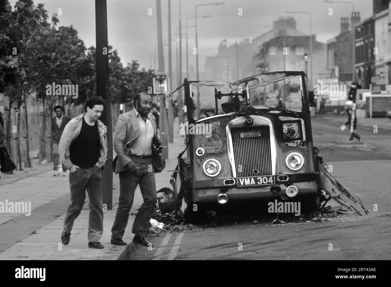 Toxteth stößt in den 1980er Jahren auf Großbritannien auf. Am Morgen nach der Nacht der Unruhen laufen zwei Männer an einem ausgebrannten und zerstörten Bus oder Van vorbei. Toxteth, Liverpool, England um Juli 1981. HOMER SYKES Stockfoto