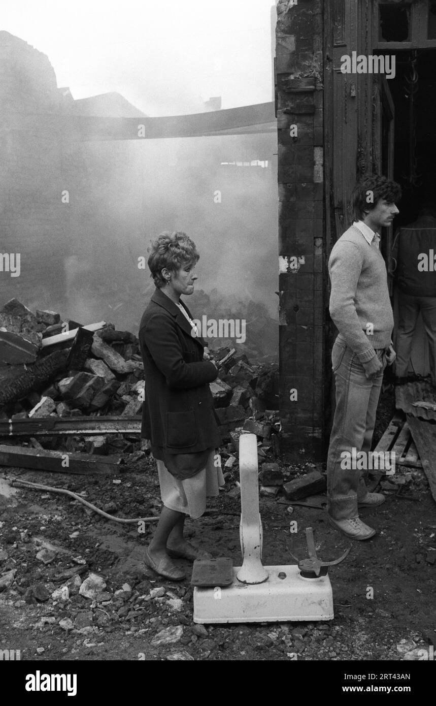 Toxteth stößt in den 1980er Jahren auf Großbritannien auf. Am Morgen nach der Nacht der Unruhen liegt eine Graswaage vor einem ausgebrannten Laden, während die Bewohner ungläubig zusehen, was mit ihrem Viertel passiert ist. Toxteth, Liverpool, England um Juli 1981. HOMER SYKES Stockfoto