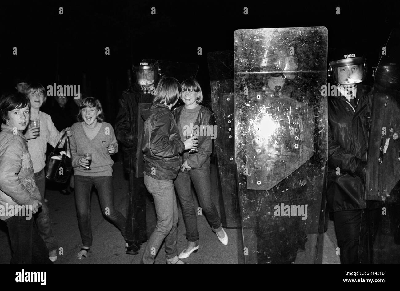 Toxteth Riots 1980s. Polizei in Aufruhr-Kleidung und Schilden. Lokale Jugendliche, Teenager hängen herum und genießen die Aufregung des Aufstands. Toxteth, Liverpool, England Juli 1981 HOMER SYKES Stockfoto