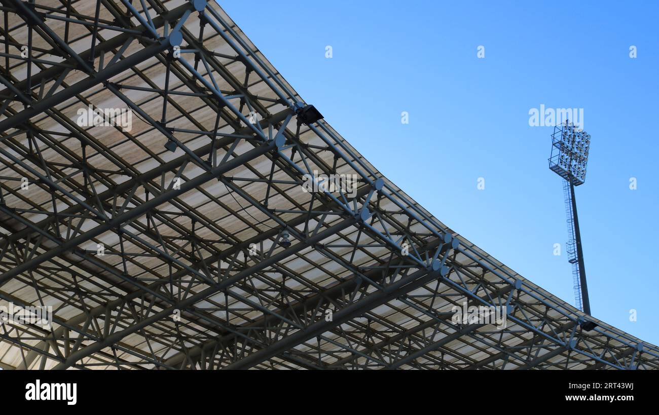 Fragment eines Stadiondaches mit einem hohen Flutlichtmast vor einem Hintergrund aus klarem blauem Himmel, Blick von unten, Elemente eines modernen urbanen Äußeren Stockfoto