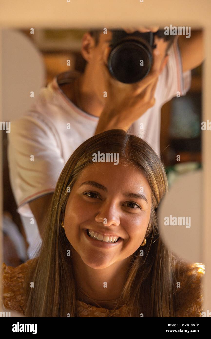 Junge Fotograf, der Fotos von seiner lächelnden Freundin durch einen Spiegel macht Stockfoto