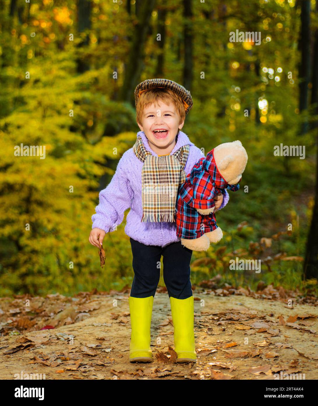 Herbstzeit. Glückliches Kind, das im Herbstpark mit Teddybär spazieren geht. Lächelndes Kind in warmer Kleidung im Herbstwald. Happy Boy in Pullover, Mütze und Schal Stockfoto
