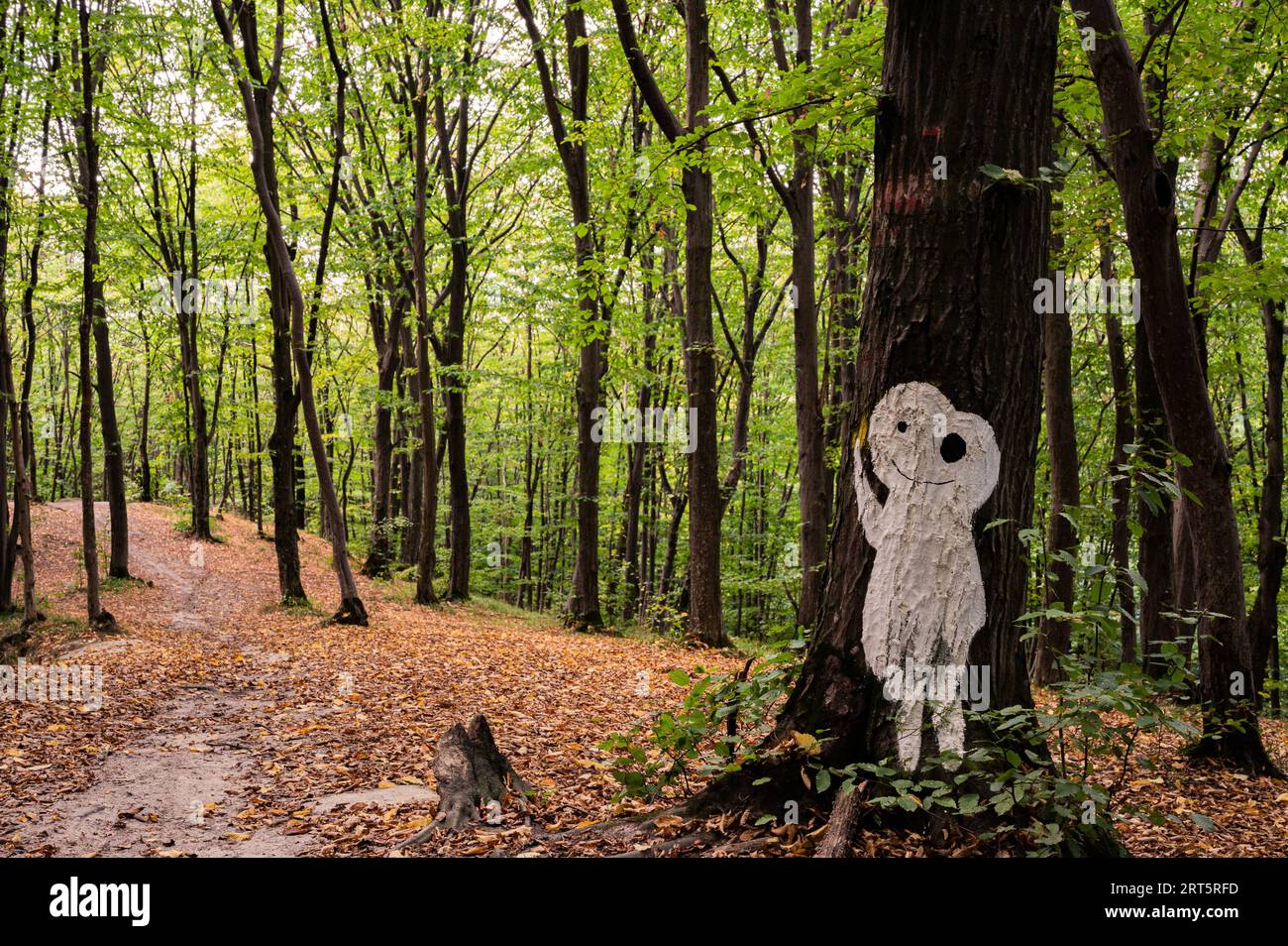 Weiße halloween-Silhuette von Mann oder Außerirdischer auf Baum im Wald abgebildet, bedeckt mit gelben trockenen Blättern, mit einer anderen solchen Silhuette auf Hintergrund. Sceni Stockfoto