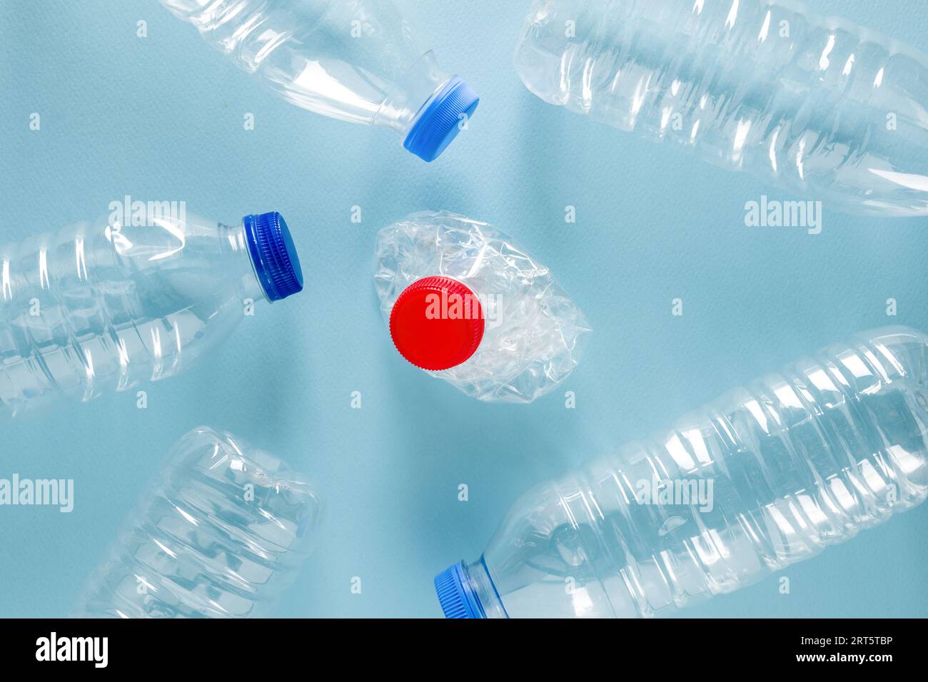 Wasserflaschen aus zerstoßenem Kunststoff mit blauen Kappen, die um die Wasserflasche aus zerstoßenem Kunststoff mit rotem Verschluss auf blauem Hintergrund stehen Stockfoto