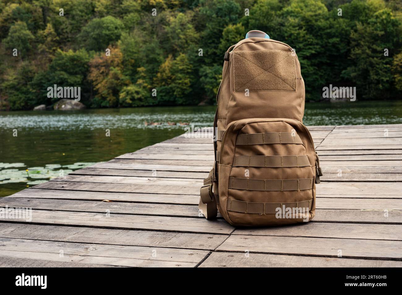 Taktischer Rucksack in Kojotenfarbe auf Holzpier am Flussufer. Tourismus, Camp, Trekking, Reisethema Stockfoto