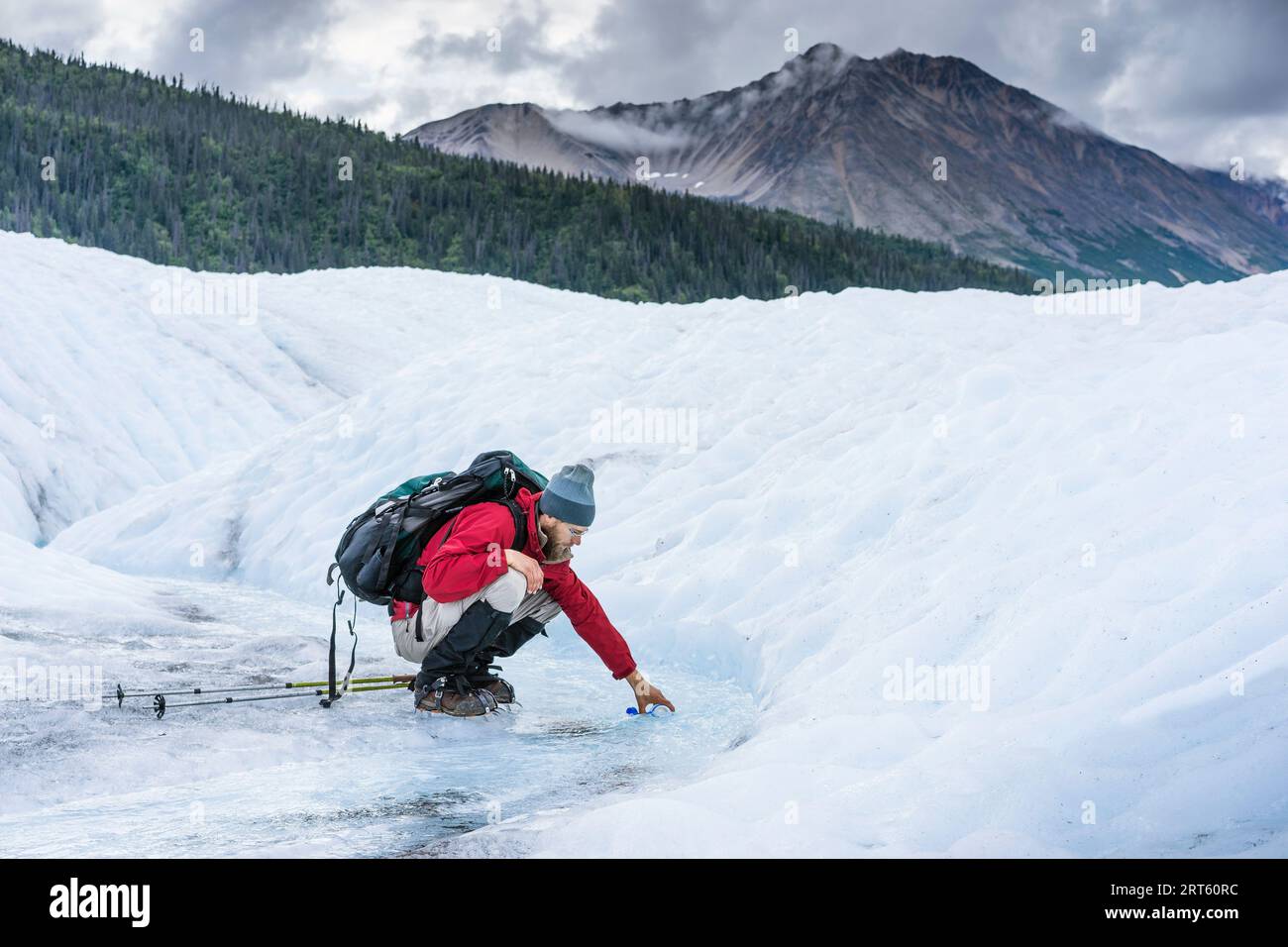 Der männliche Wanderer sammelt Wasser aus dem Gletscherbach auf dem Gletscher Wrangell Stockfoto