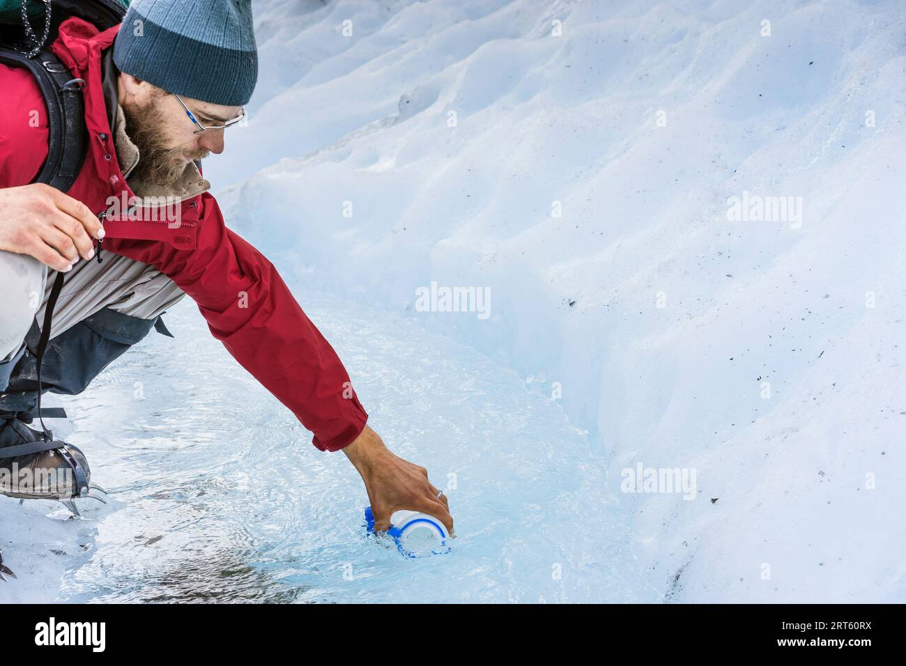 Der männliche Wanderer sammelt Wasser aus dem Gletscherbach auf dem Gletscher Wrangell Stockfoto
