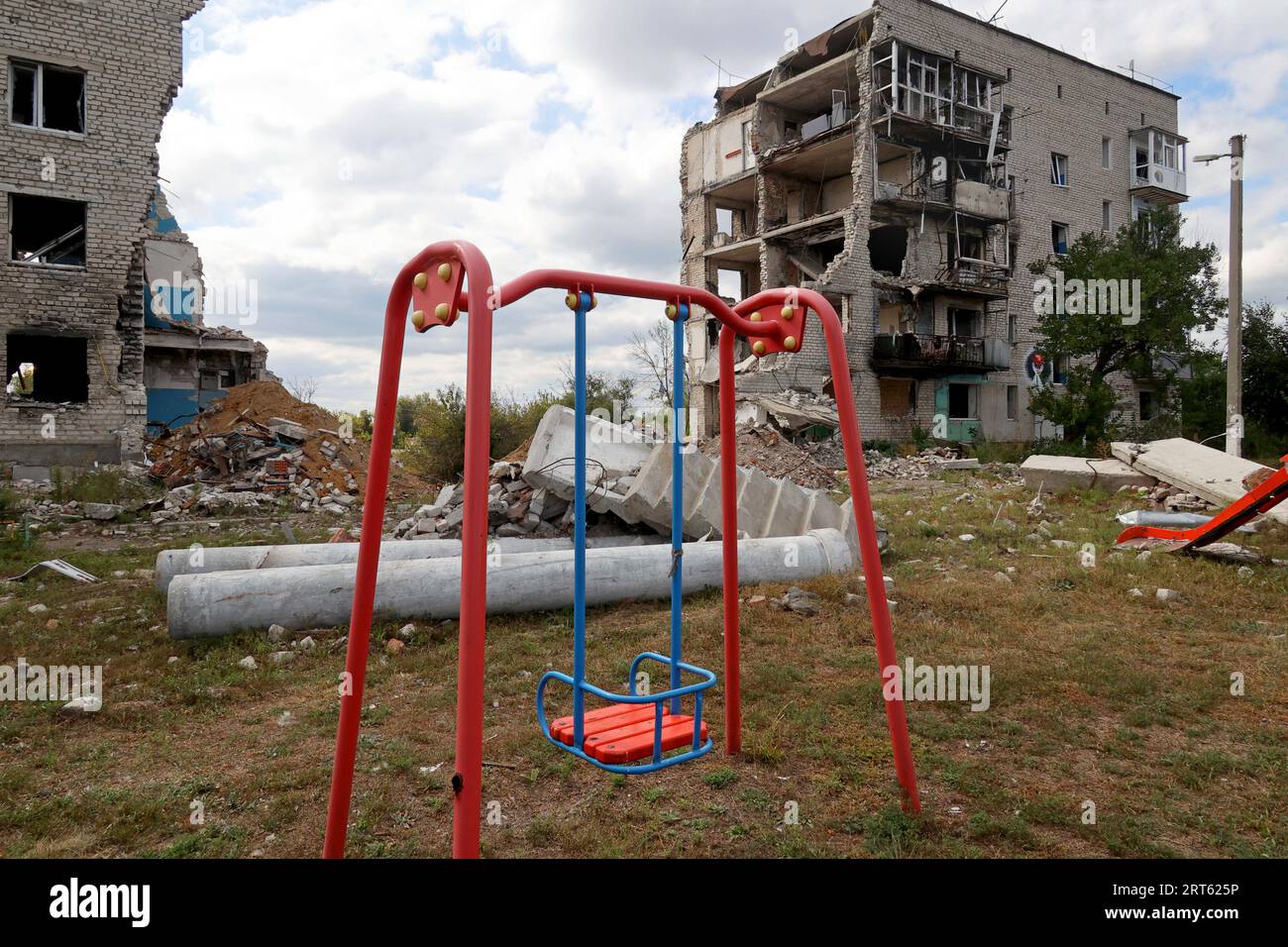 IZIUM, UKRAINE - 10. SEPTEMBER 2023 - Eine Schaukel ist vor einem Wohnblock abgebildet, der durch die Beschießung russischer Truppen ruiniert wurde, wie auf der ersten ann zu sehen war Stockfoto