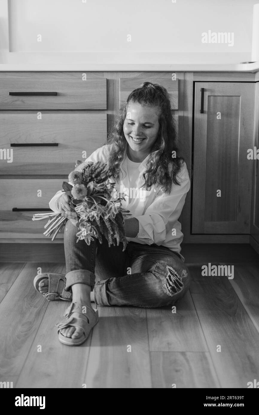 Ein Blumenhändler, der auf ihrem Küchenboden sitzt und einen Blumenstrauß fres hält Stockfoto