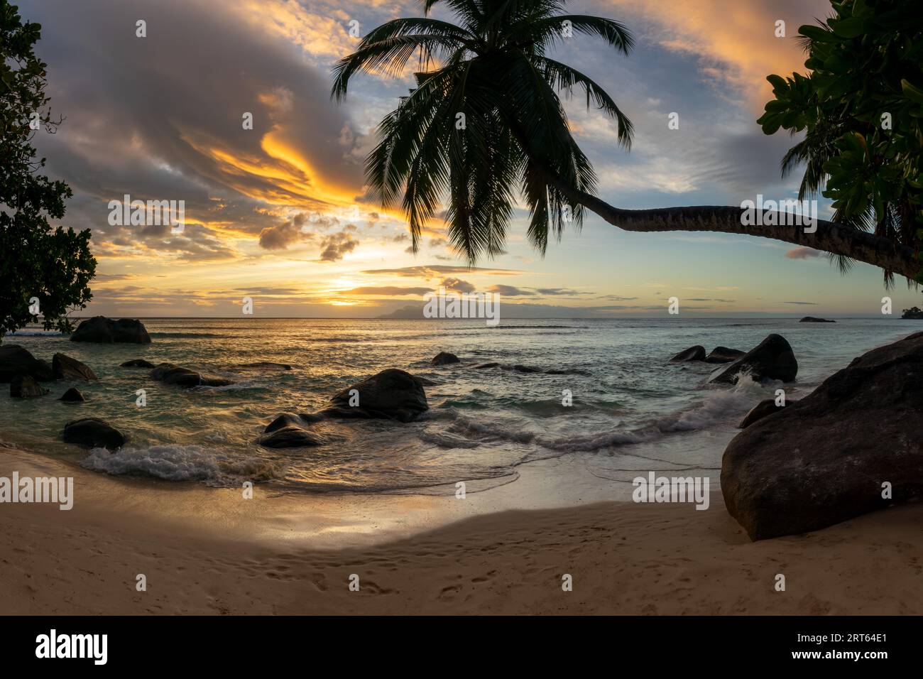 Perfekte Sonnenuntergangslandschaft an einem malerischen tropischen Sandstrand mit Palmen und Felsbrocken auf der Insel Mahé, Seychellen Stockfoto