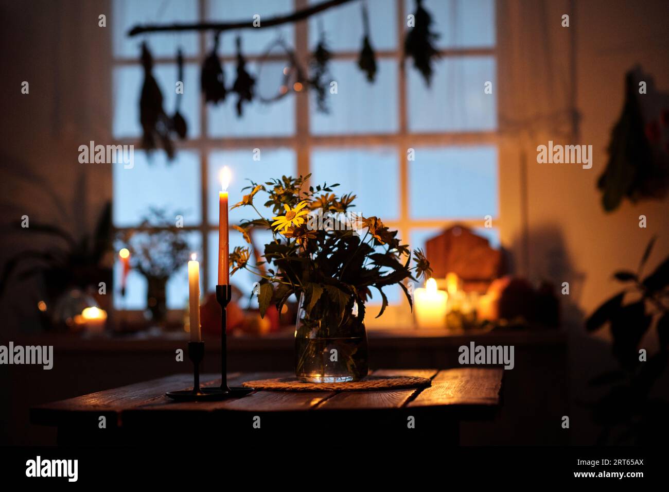 Zwei Kerzenleuchter mit brennenden Kerzen stehen auf einem Holztisch neben einer Vase mit einem Haufen gelber Gartenblumen an der Küchenzeile Stockfoto Zwei Kerzenleuchter mit brennenden Kerzen stehen auf einem Holztisch neben einer Vase mit einem Haufen gelber Gartenblumen an der Küchenzeile Stockfoto