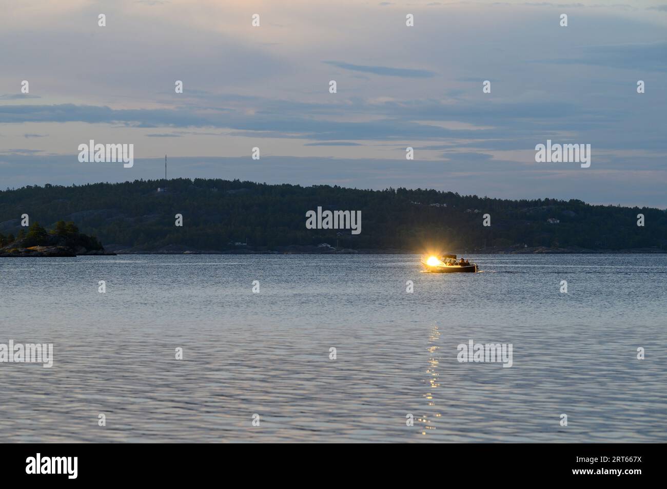 Die Abendsonne spiegelt sich in der Windschutzscheibe eines traditionellen Freizeitbootes wider, das über das Meer segelt, mit der Insel Fluer im Hintergrund, Telemark, Norwegen. Stockfoto