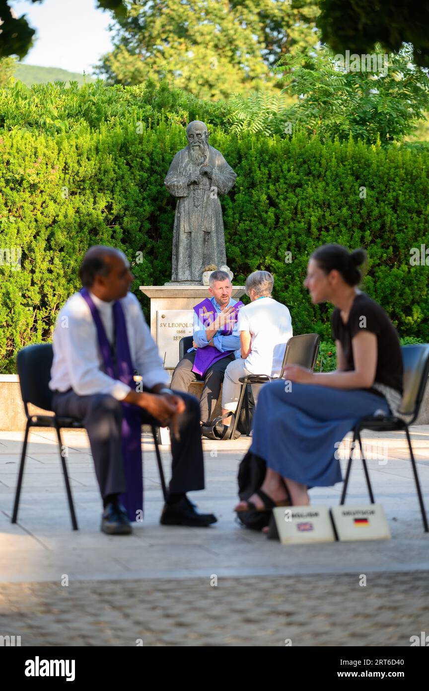 Pilger, die in Medjugorje gestehen. Im Hintergrund steht die Statue des Heiligen Leopold Mandić – Schutzpatron der Beichtleute. Stockfoto