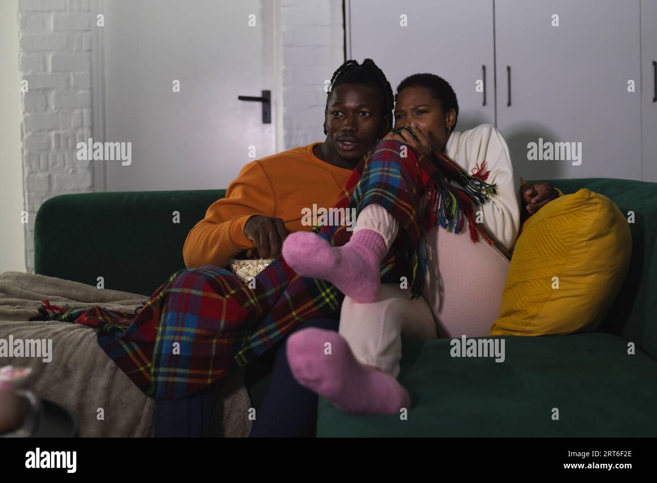 Ängstliches afroamerikanisches Paar, das sich zu Hause entspannt, fernsieht und Popcorn isst Stockfoto
