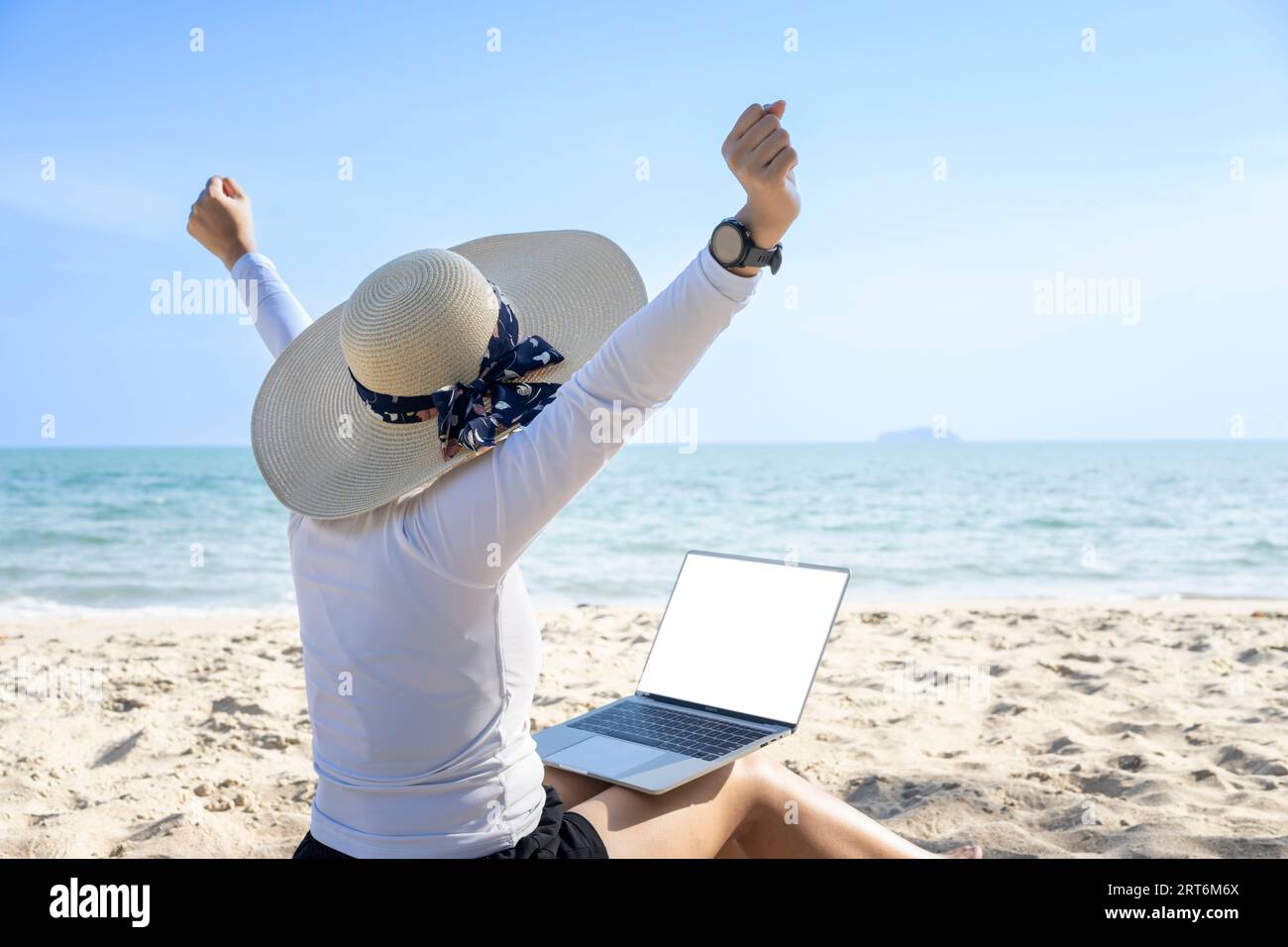 „Work from Anywhere“-Konzept. Rückansicht einer jungen Frau, die am Strand mit einem Computer-Laptop arbeitet Stockfoto