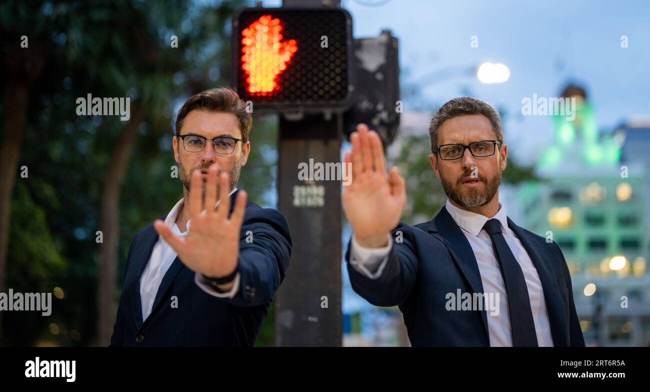 Zwei gutaussehende Geschäftsleute im Anzug hören auf mit der Hand zu singen. Warnausdruck mit negativer und ernsthafter Geste im Gesicht. Halten Sie die Handbewegung an Stockfoto