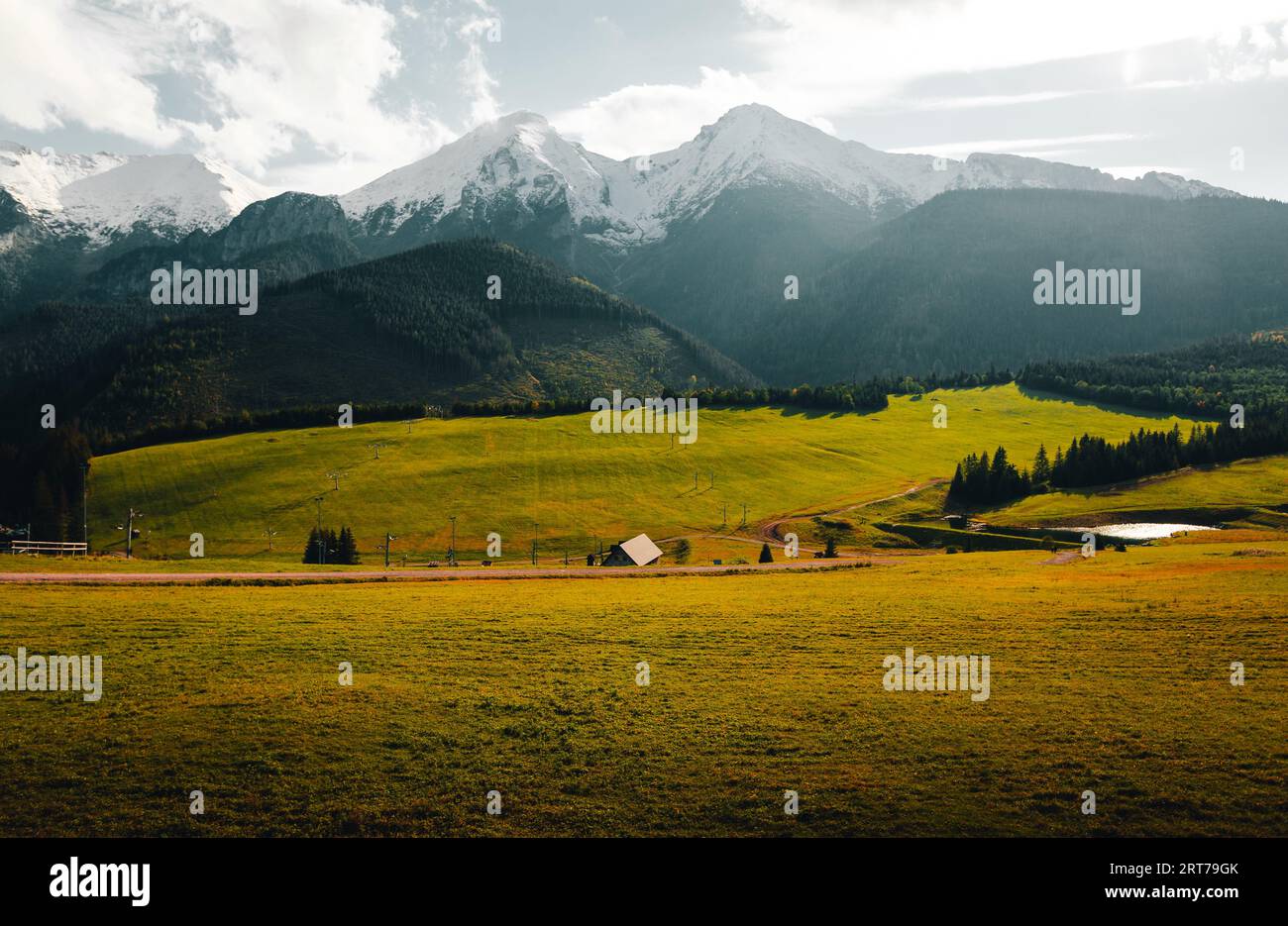 Landschaftsfotografie von Herbstwiese mit kleiner Hütte und See mit einem wunderschönen schneebedeckten Berggipfel im Hintergrund. Wunderschönes natürliches Sonnenlicht Stockfoto