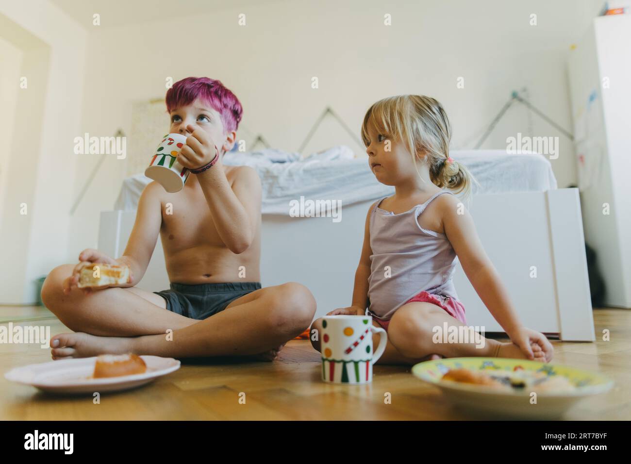 Geschwister sitzen auf dem Boden und essen einen Snack im Kinderzimmer. Stockfoto