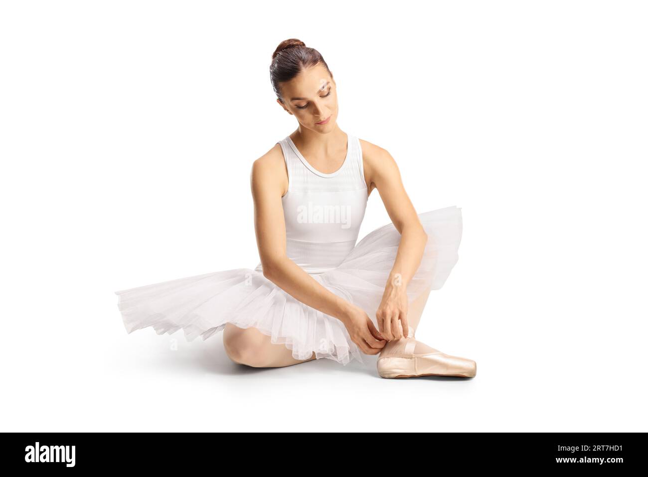 Ballerina in einem weißen Kleid sitzend und Ballettschuhe auf weißem Hintergrund bindend Stockfoto