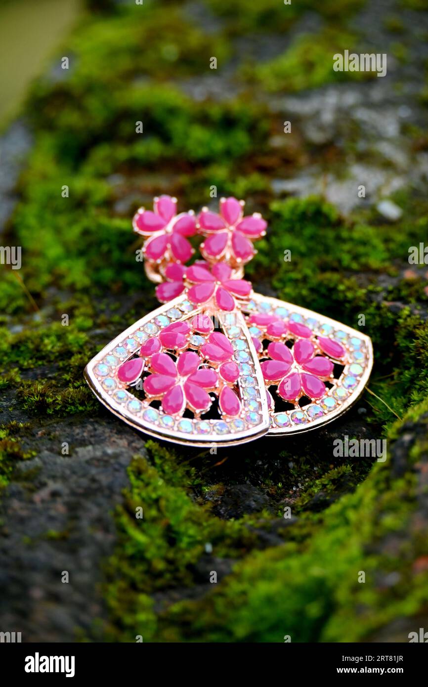 Schließen Sie das Paar rosa silberfarbene Ohrringe auf dem grünen Gras Soft Focus natürlichen grünen braunen Hintergrund. Stockfoto