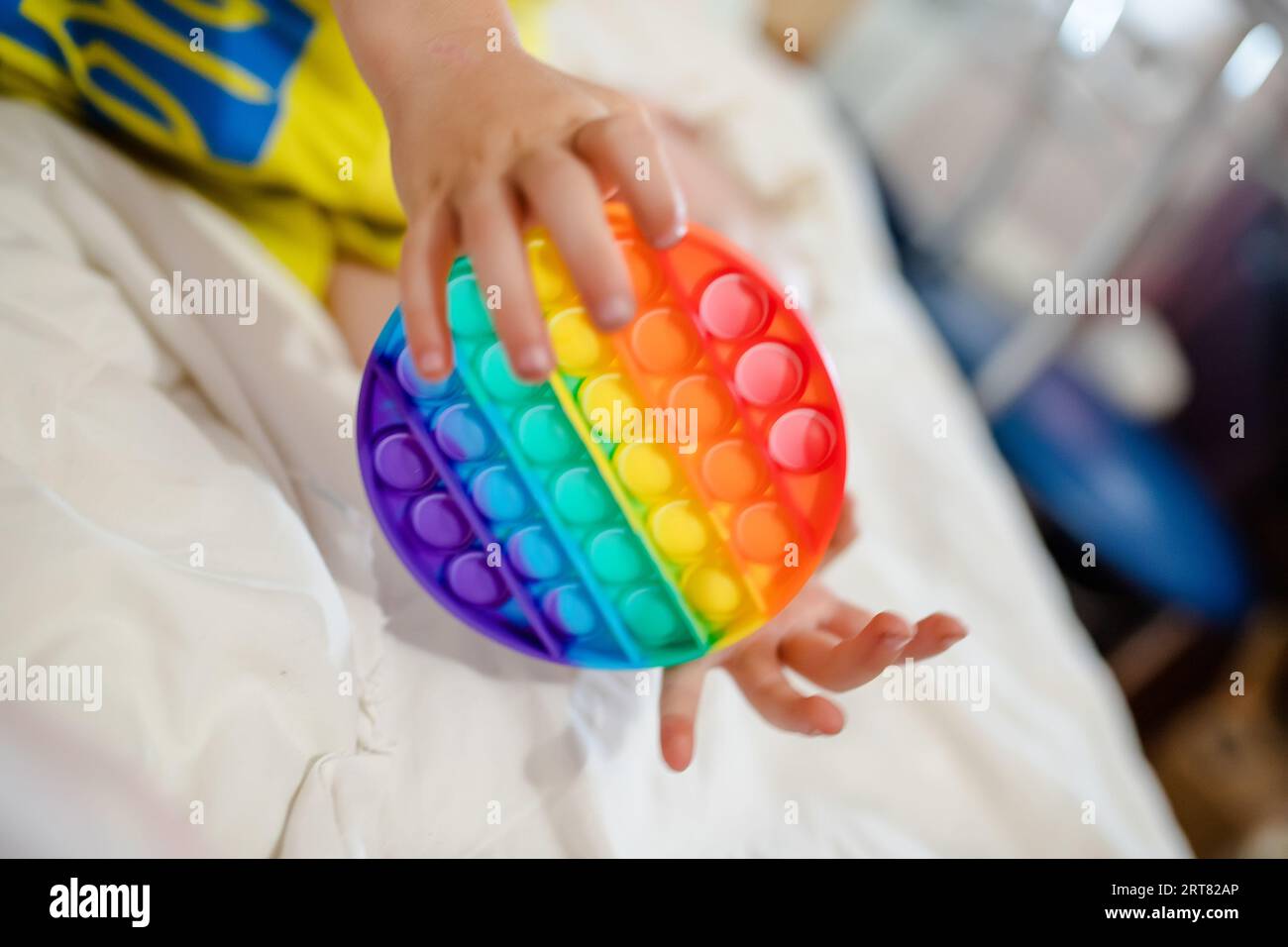 Die Hände des Kleinkindes halten ihn fest. Ein fröhliches Kind auf dem Bett mit einem Anti-Stress-Spielzeug. Weiche Stofftiere mit Blasen. Kind spielt mit Stockfoto