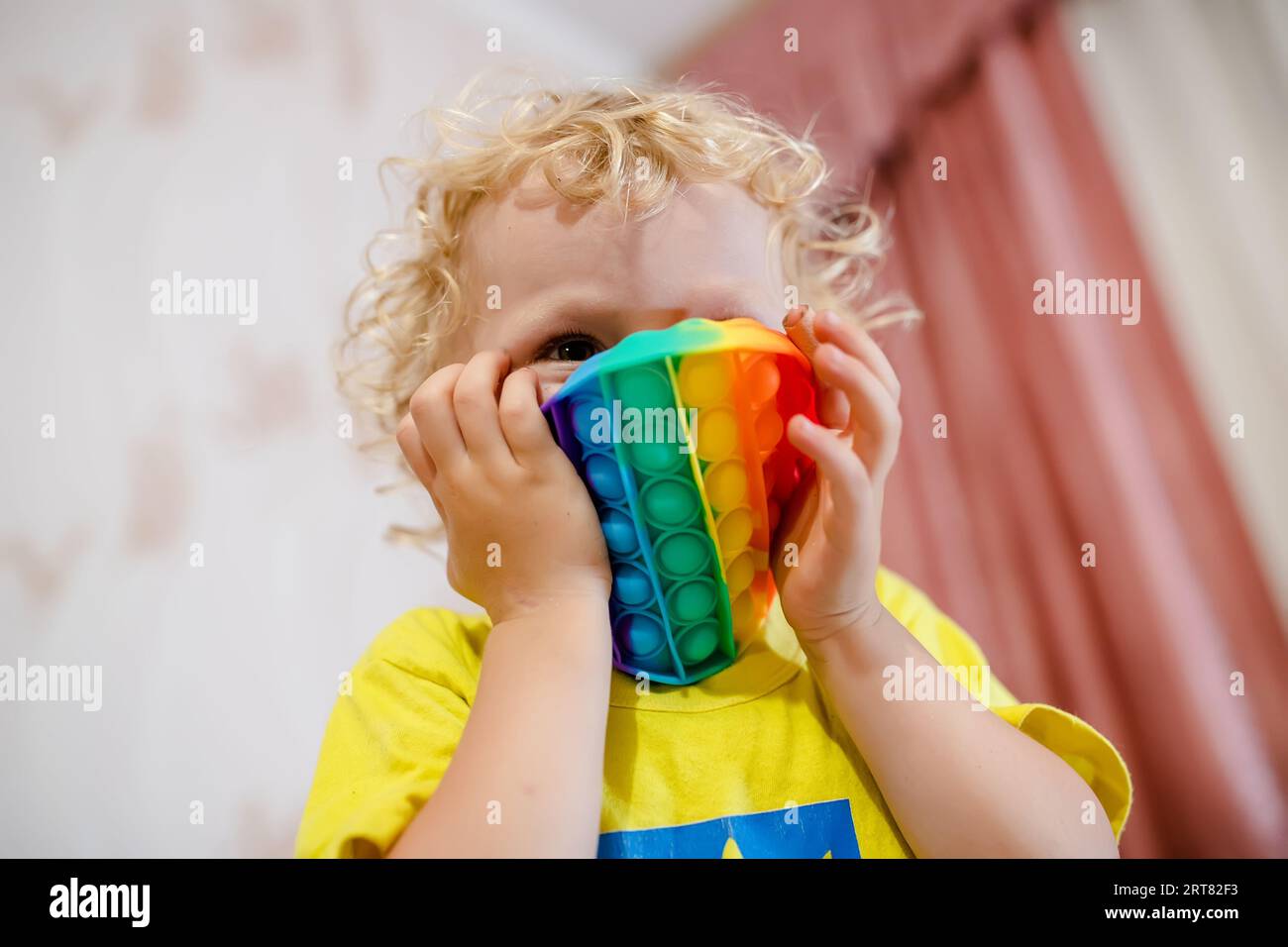 Weiche Stofftiere mit Blasen. Das Kind spielt mit dem Regenbogenpop-it in Form eines Kreises Stockfoto