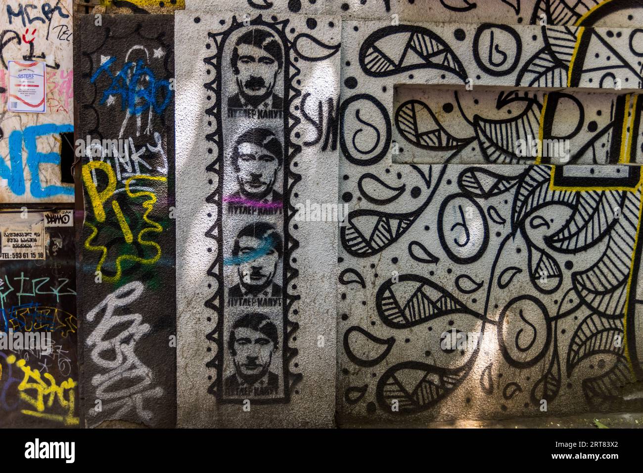 Gezeichnete Männer, die Putin und Hitler ähneln, werden als Graffiti in einer vertikalen Reihe an einer Wand dargestellt. Unter einigen der Flächen befindet sich der Text „ПУТИН ХУЙЛО“. Die Wand ist mit weiteren Graffiti und Mustern bedeckt. Das Graffiti befindet sich in Chugureti, Tiflis, Georgien Stockfoto
