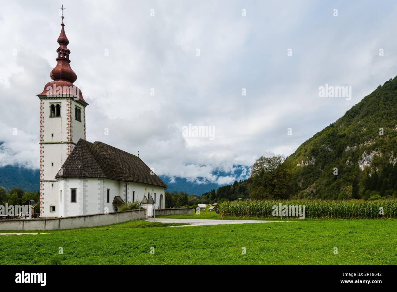 Schöne alte einsame Kirche mit angrenzendem Friedhof im Bergtal Mit frischem Gras und bewölktem Himmel inmitten hoher Berggipfel Stockfoto