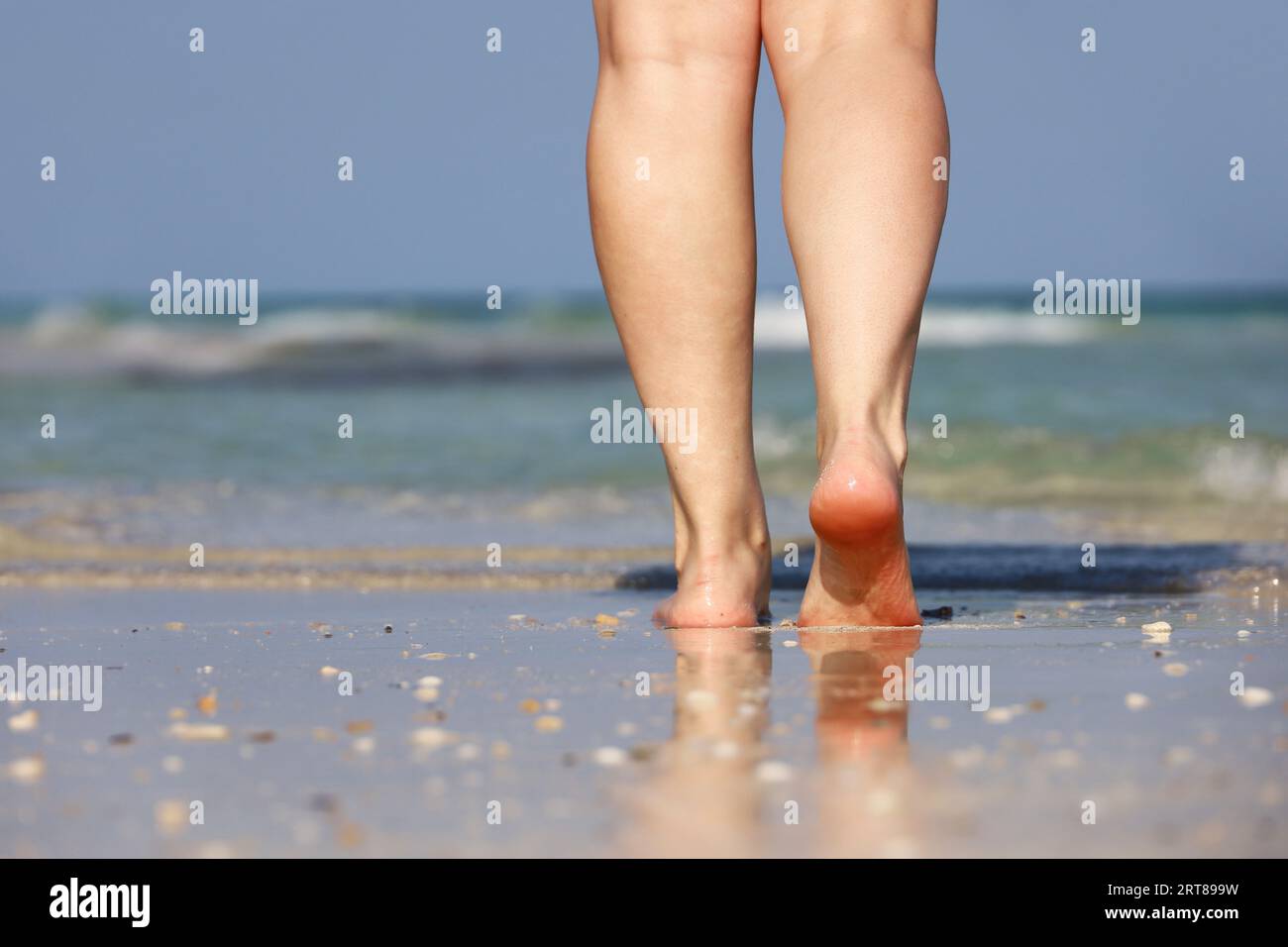 Barfußmädchen, das am Sand auf Meereswellen im Hintergrund spaziert. Weibliche Beine aus nächster Nähe, Strandurlaub Stockfoto