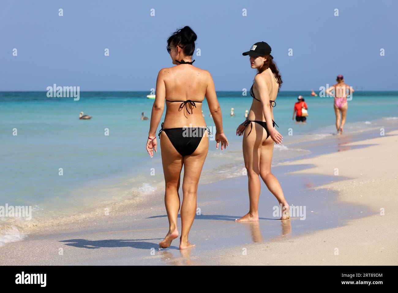 Zwei junge Frauen im Bikini, die am tropischen Strand durch den Sand laufen. Ocean Coast, Touristenresort auf der Karibikinsel Stockfoto