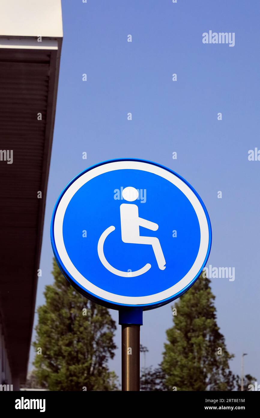 Behindertenparkplatz auf der runden Seite - Mann im Rollstuhl vor blauem Hintergrund, der Parkplätze in der Nähe von Eingängen anzeigt, um Zugang zu erhalten Stockfoto