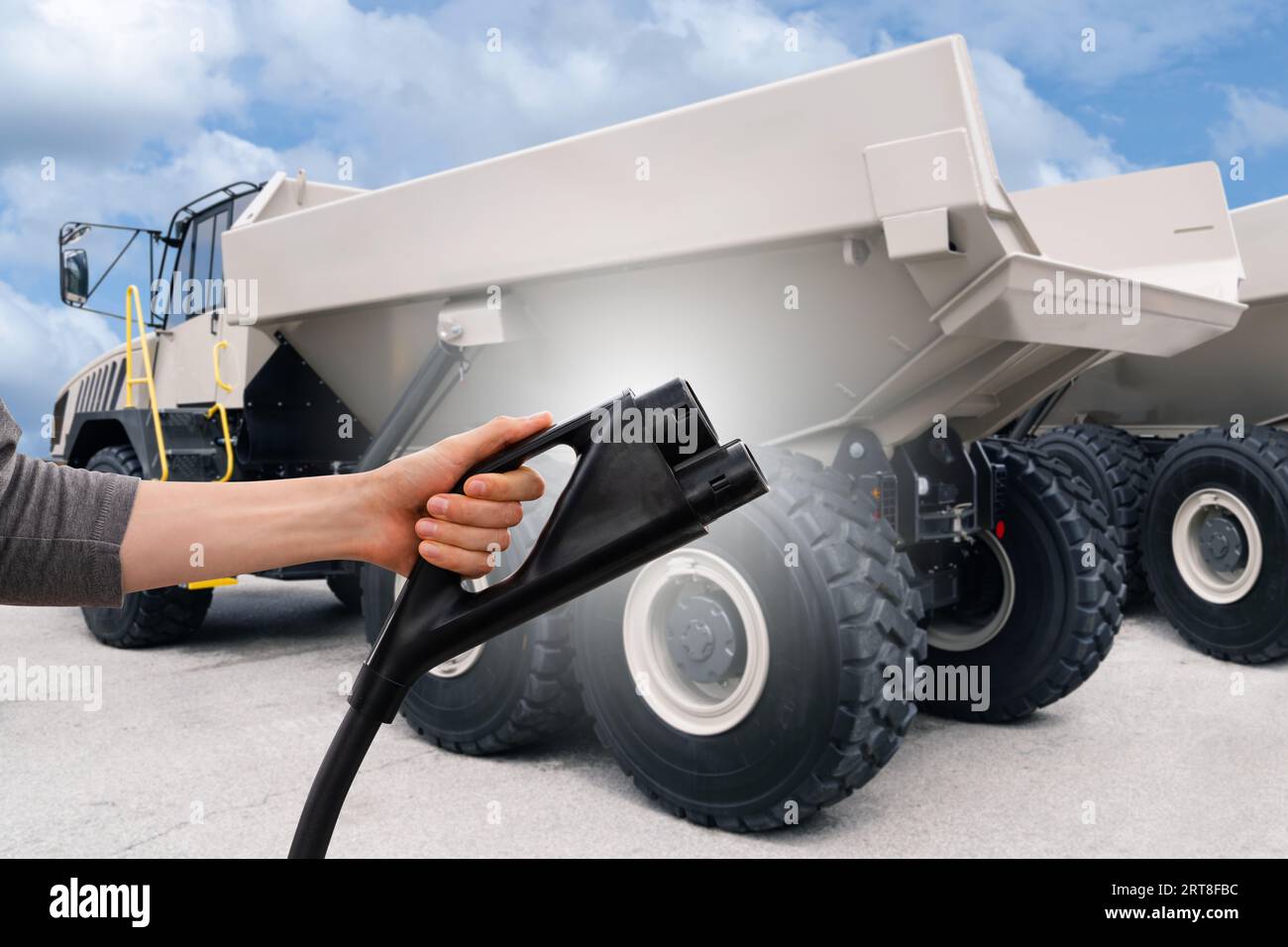 Hand mit Ladestecker auf einem Hintergrund eines Elektrobergbauwagens. Konzept... Stockfoto