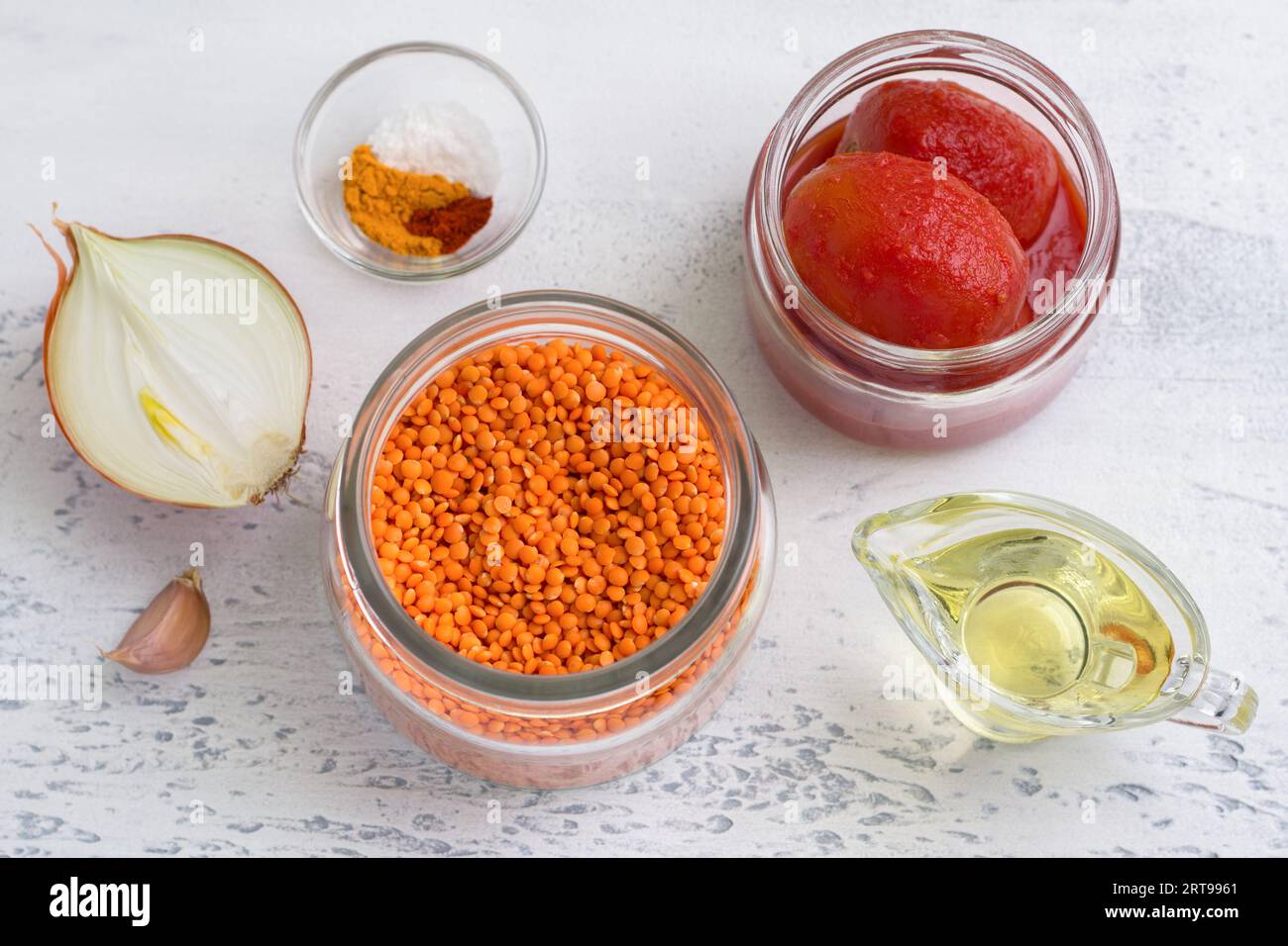 Zutaten für vegane Tomatenlinsensauce, Suppe oder für Linsenpfannkuchen: Rote Linsen, Zwiebeln, Knoblauch, Tomaten in Dosen, Gewürze und Pflanzenöl auf einem li Stockfoto