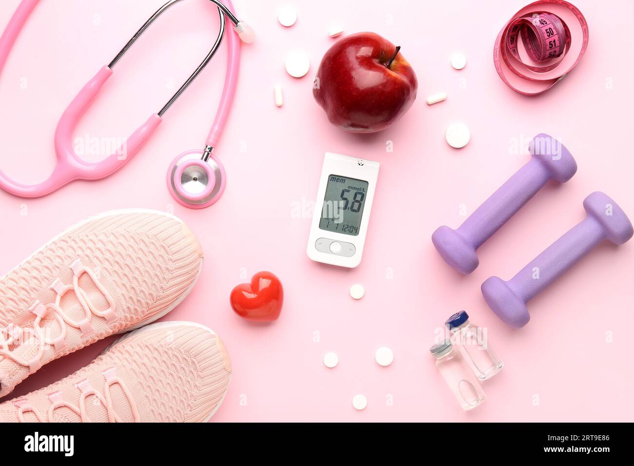 Glucometer, Turnschuhe, Apfel, Kurzhanteln und Pillen auf rosafarbenem Hintergrund. Diabetes-Konzept Stockfoto