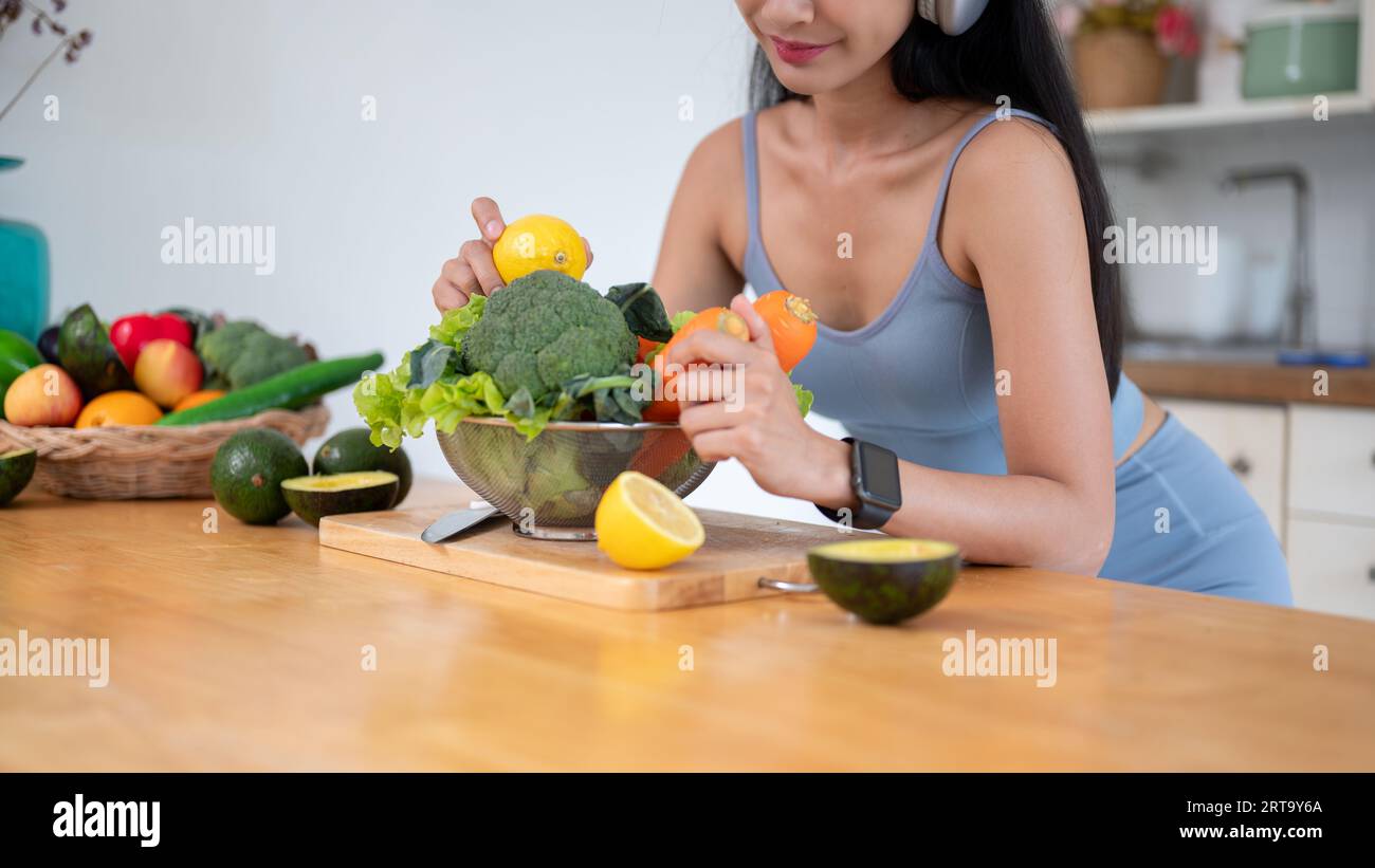 Abgeschnittenes Bild einer schönen jungen asiatischen Frau in Fitnesskleidung bereitet frische Zutaten für ihr gesundes Frühstück nach dem Fitnessstudio an einem Tisch im vor Stockfoto