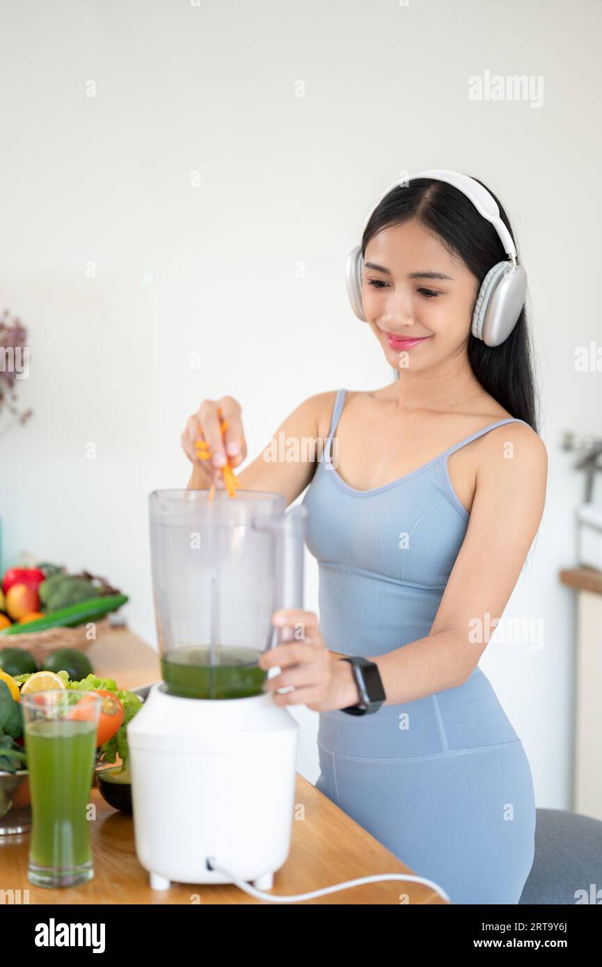 Ein Porträt einer wunderschönen und fitten jungen asiatischen Frau in Turnkleidung macht ihren gesunden Smoothie in der Küche zum Frühstück nach dem Fitnessstudio. Stockfoto